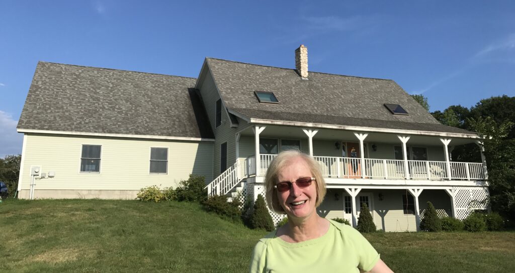 Homeowner standing in front of her house with elevated porch and finished basement, showcasing completed foundation and exterior improvements