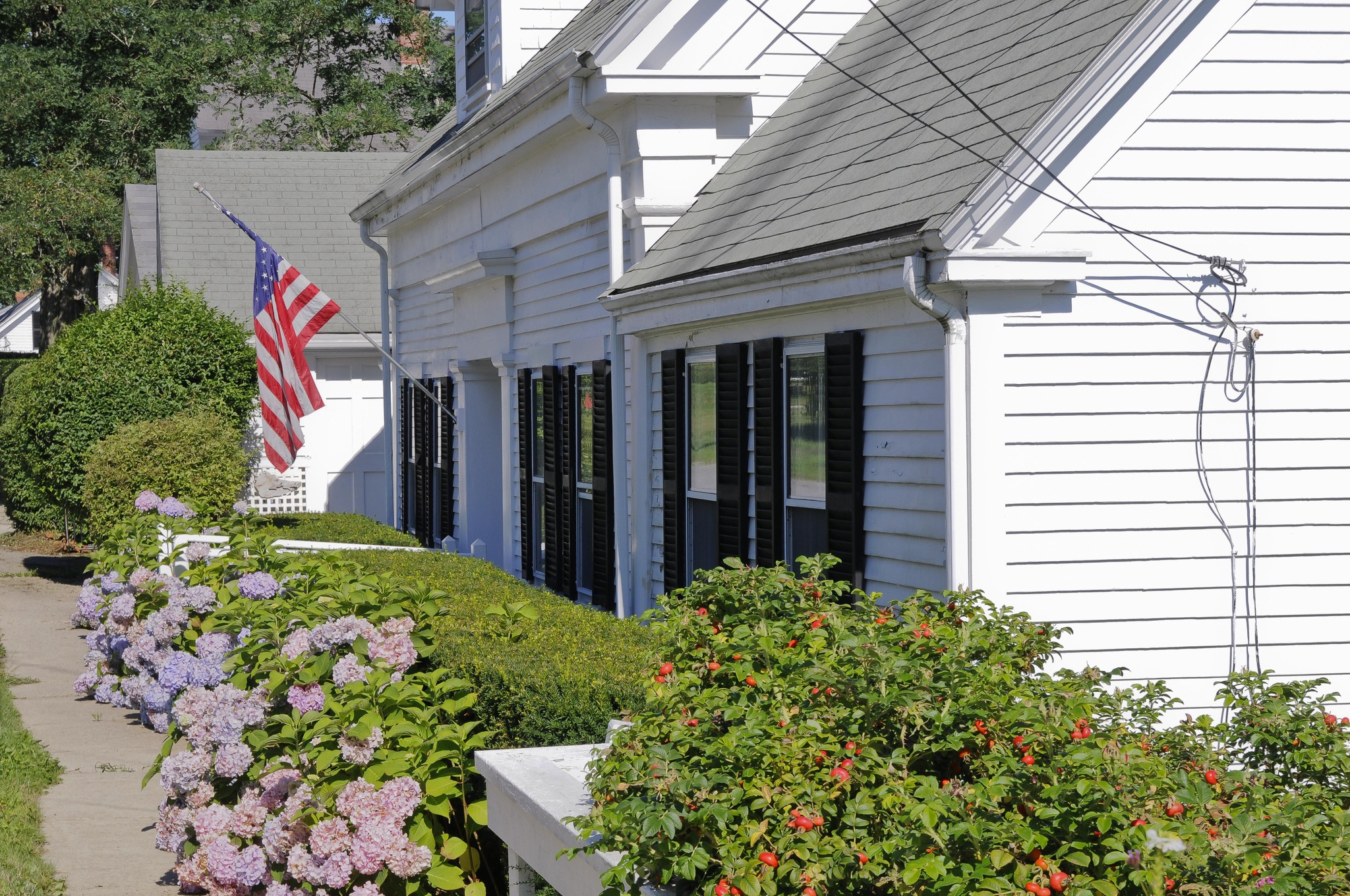 White Cape House With American Flag Hanging Out Front