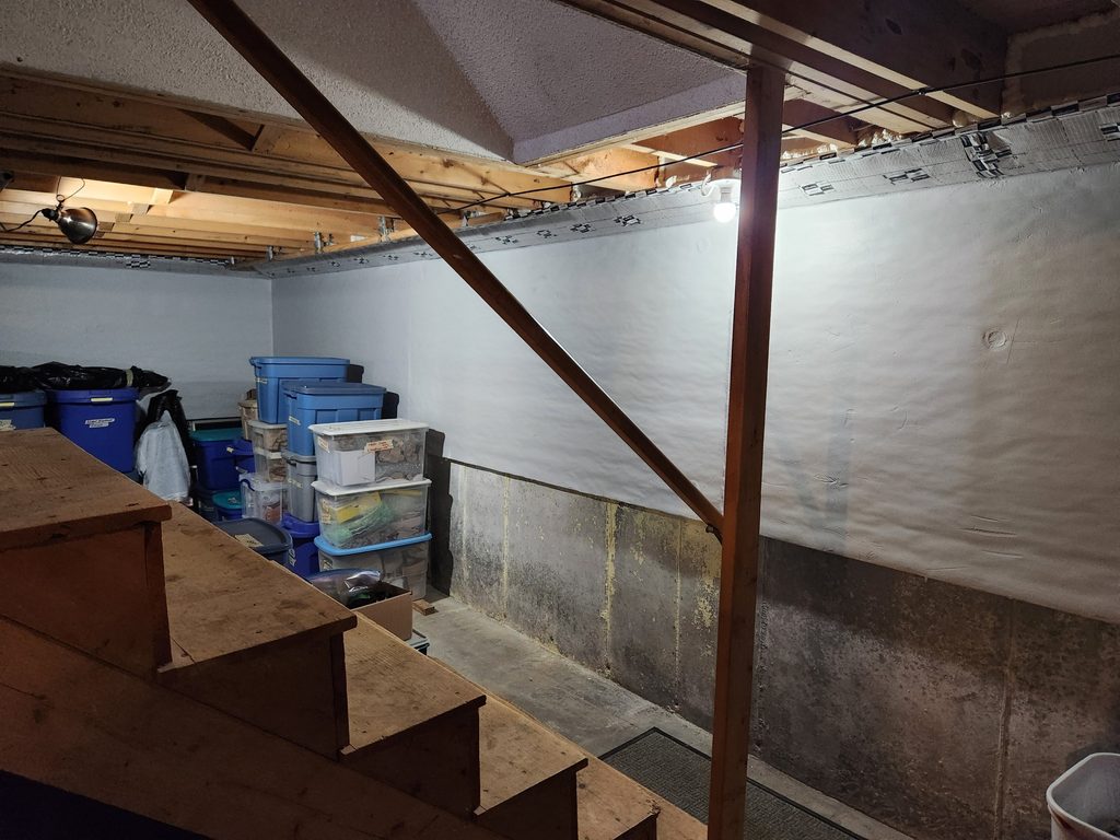 Basement wall covered in white rigid foam with a sealed rim joist above, after rim joist and basement wall insulation in Freeport, Maine