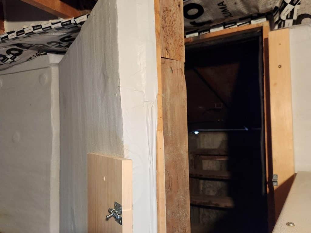 Basement door insulated with white foam board and a wood latch, with mineral wool and tape above the door frame