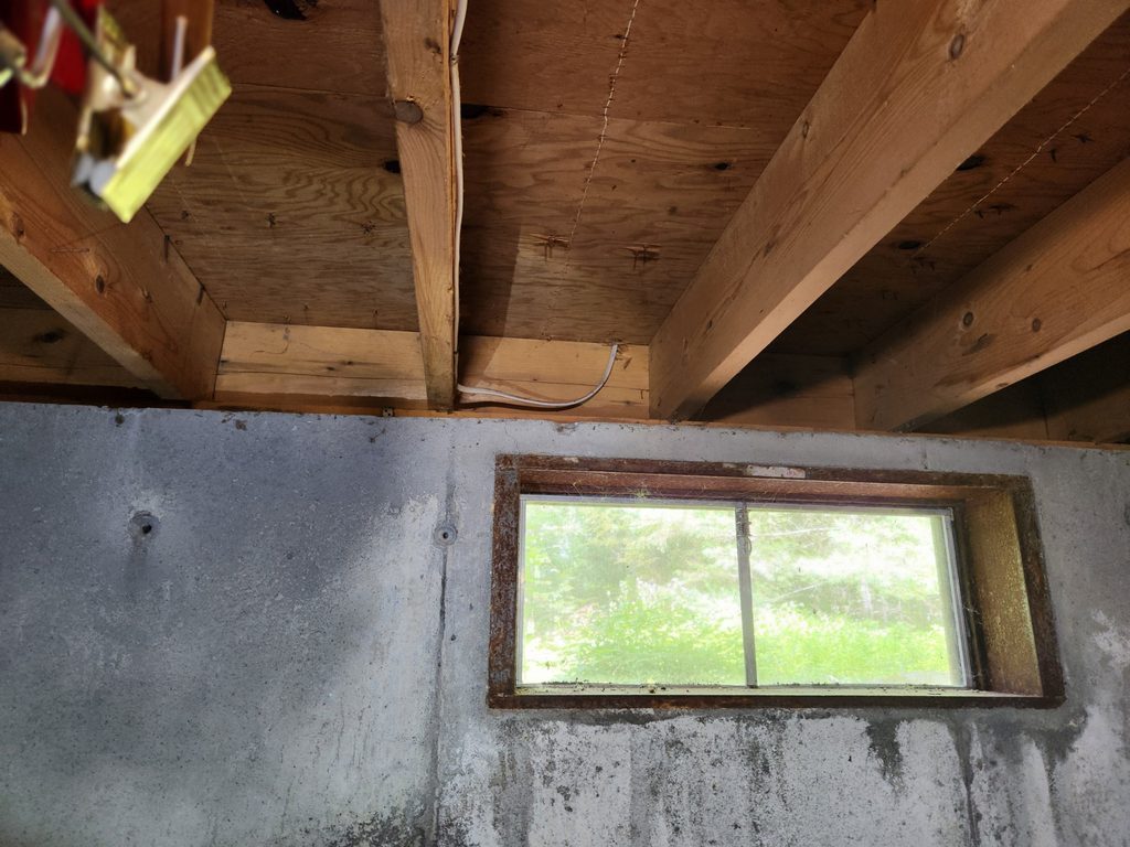 Open rim joist bays above a bare concrete basement wall before insulation in a Freeport, Maine home
