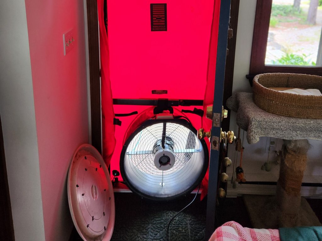 Blower door fan mounted in a doorway with a red panel during an air leakage test