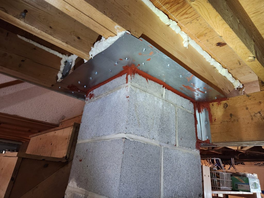Chimney chase sealed with sheet metal and red fire-rated caulk where it meets the basement floor framing