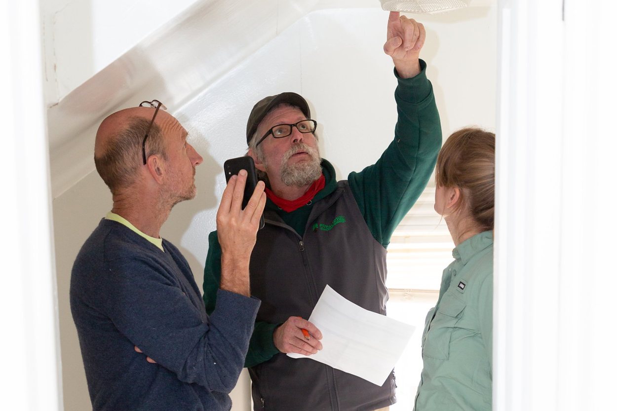 Three people looking up at a ceiling light fixture while an Evergreen energy advisor points to it during a home energy audit