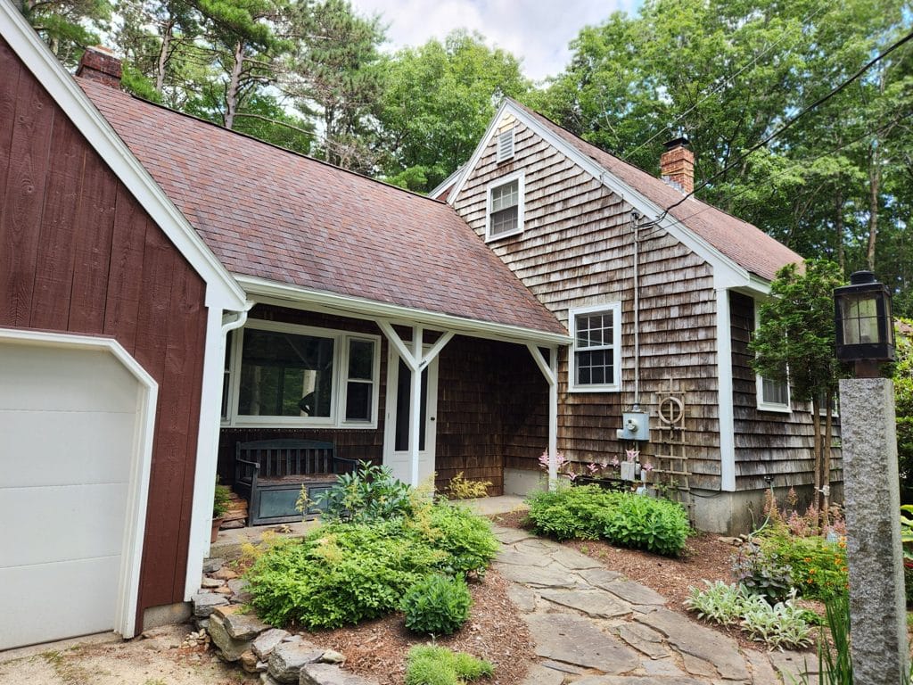 Front entry of a Freeport, Maine cape with cedar shingles, a covered porch, and a stone walkway through the garden