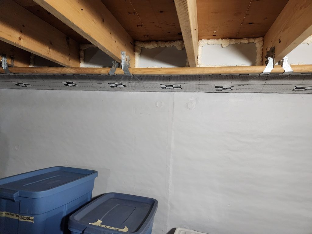 Rim joist insulation sealed with foam and air barrier tape along the top of a basement wall in Freeport, Maine